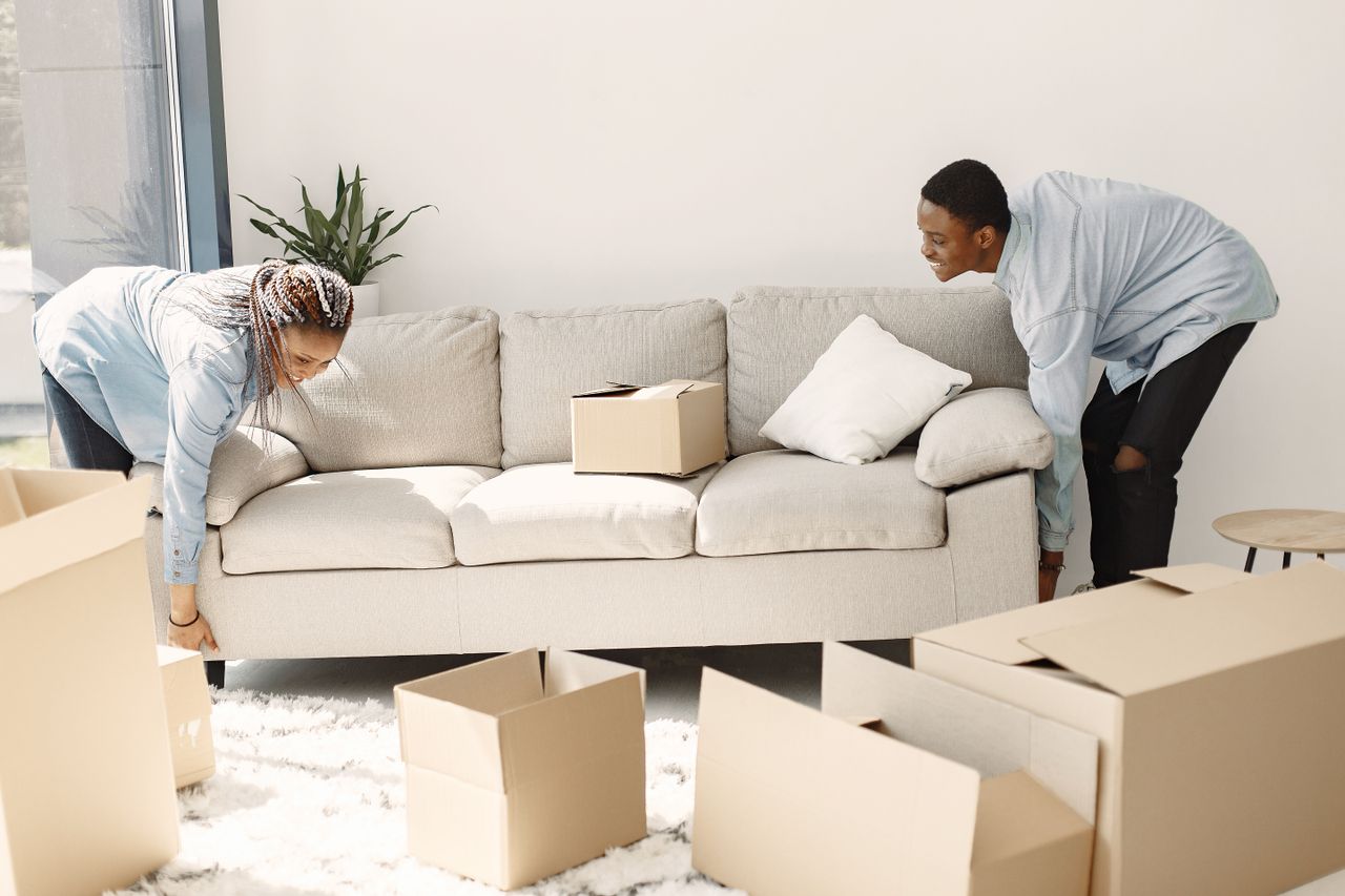 Joyful couple arranging a sofa in their new house, with moving boxes all around them.
